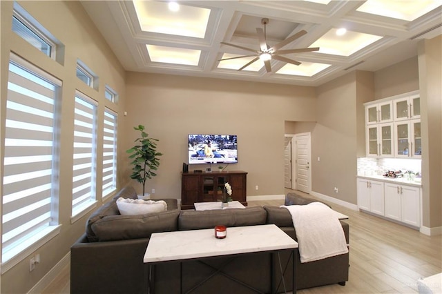 living room with coffered ceiling, light wood-type flooring, ceiling fan, a towering ceiling, and beam ceiling