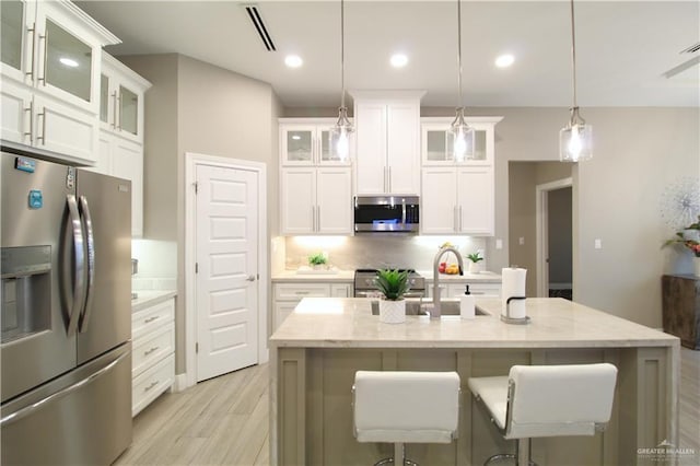 kitchen featuring an island with sink, appliances with stainless steel finishes, pendant lighting, and white cabinets