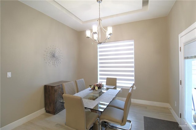 dining room with a notable chandelier, light hardwood / wood-style floors, and a raised ceiling