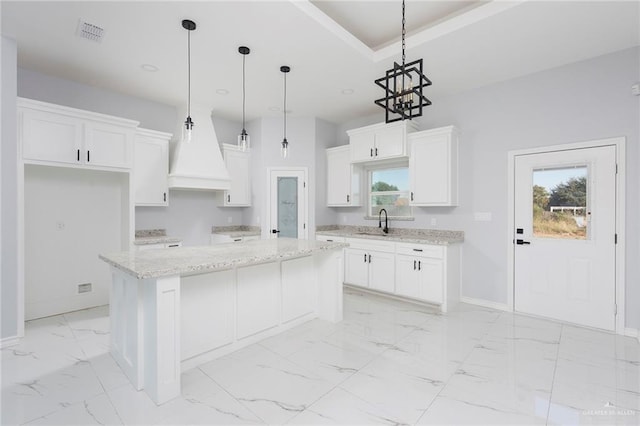 kitchen featuring white cabinetry, a center island, sink, hanging light fixtures, and light stone counters