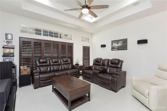 tiled living room featuring a raised ceiling, a high ceiling, and ceiling fan