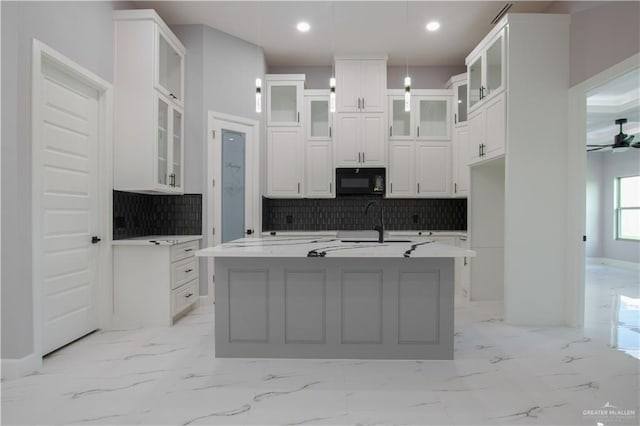 kitchen with white cabinets, a center island with sink, ceiling fan, tasteful backsplash, and decorative light fixtures