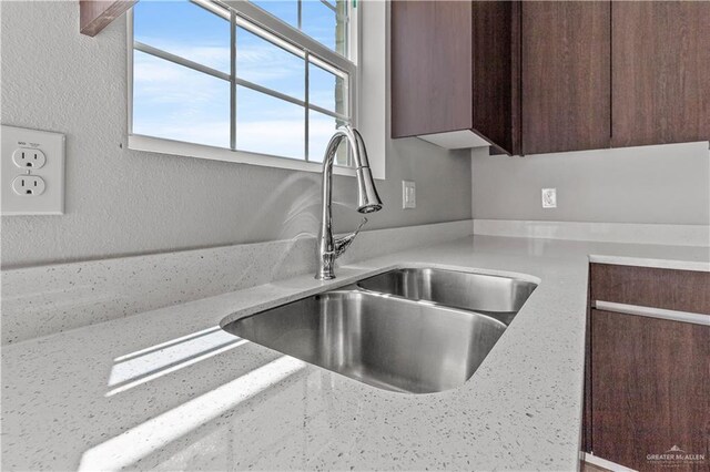 kitchen featuring dark brown cabinetry, light stone counters, and sink