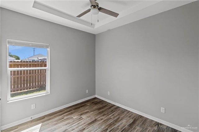 empty room with hardwood / wood-style floors, a raised ceiling, and ceiling fan