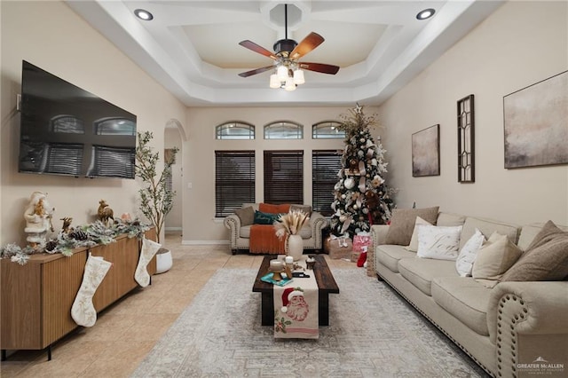 tiled living room with a raised ceiling, ceiling fan, and a towering ceiling