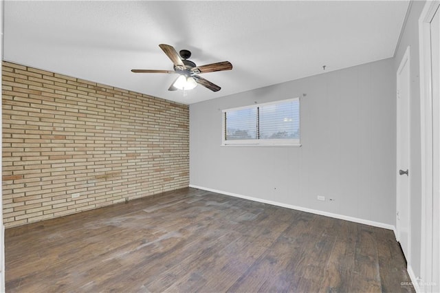 spare room featuring dark hardwood / wood-style floors, ceiling fan, and brick wall