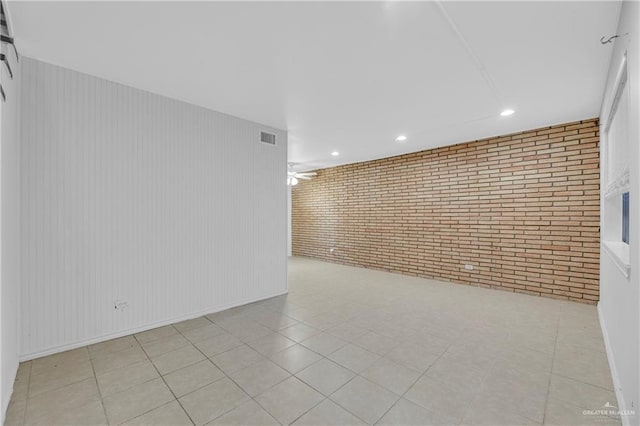 tiled empty room featuring ceiling fan and brick wall