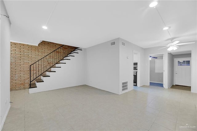 unfurnished living room featuring ceiling fan and brick wall