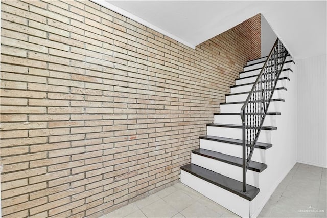 stairs with tile patterned floors and brick wall