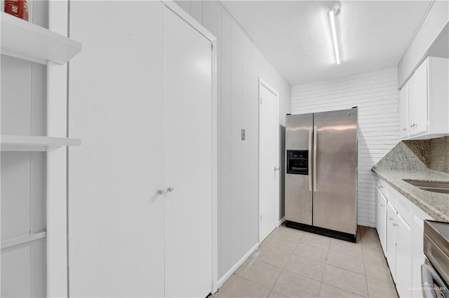 kitchen with white cabinets, light tile patterned flooring, light stone countertops, and stainless steel appliances