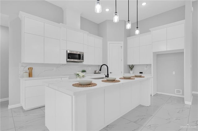 kitchen with sink, white cabinetry, tasteful backsplash, an island with sink, and pendant lighting