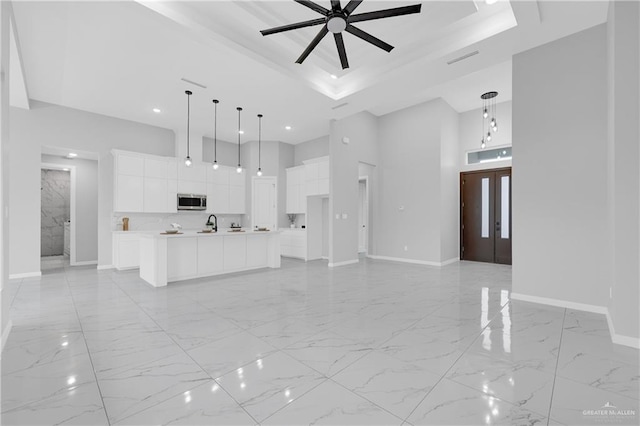 kitchen featuring a raised ceiling, hanging light fixtures, an island with sink, and white cabinets