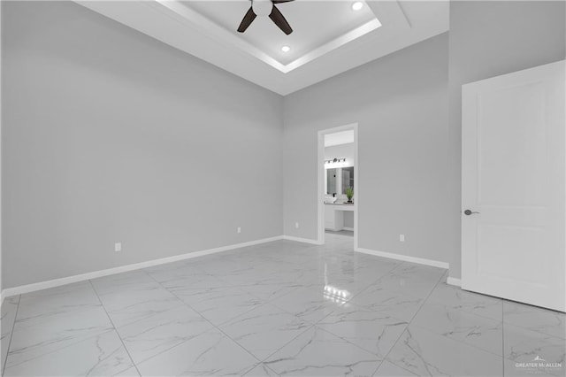 empty room with a tray ceiling, ceiling fan, and a towering ceiling