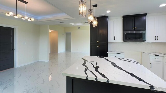 kitchen featuring a raised ceiling, light stone counters, white cabinets, and pendant lighting