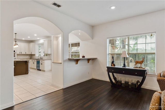 kitchen with white cabinets, sink, hanging light fixtures, stainless steel dishwasher, and light wood-type flooring