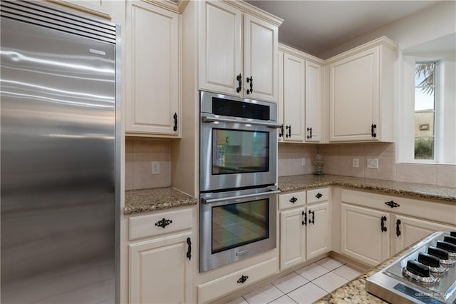 kitchen featuring decorative backsplash, light stone countertops, stainless steel appliances, and light tile patterned floors