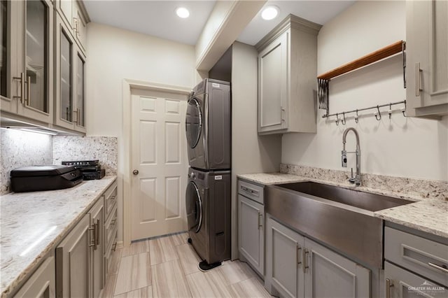 kitchen with light stone countertops, backsplash, gray cabinetry, sink, and stacked washer / drying machine