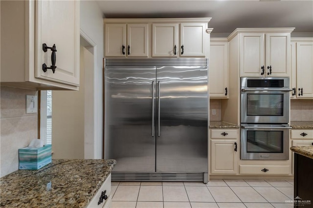 kitchen featuring appliances with stainless steel finishes, tasteful backsplash, light tile patterned floors, stone countertops, and cream cabinetry