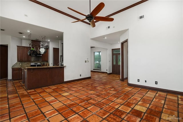 kitchen featuring ceiling fan, tasteful backsplash, kitchen peninsula, a towering ceiling, and ornamental molding