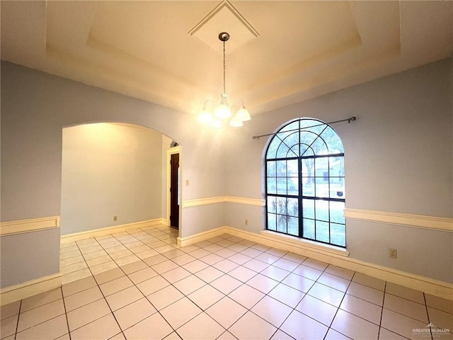 tiled spare room with a raised ceiling and a chandelier