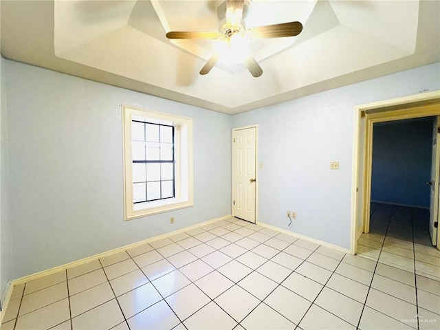 tiled empty room featuring a tray ceiling and ceiling fan