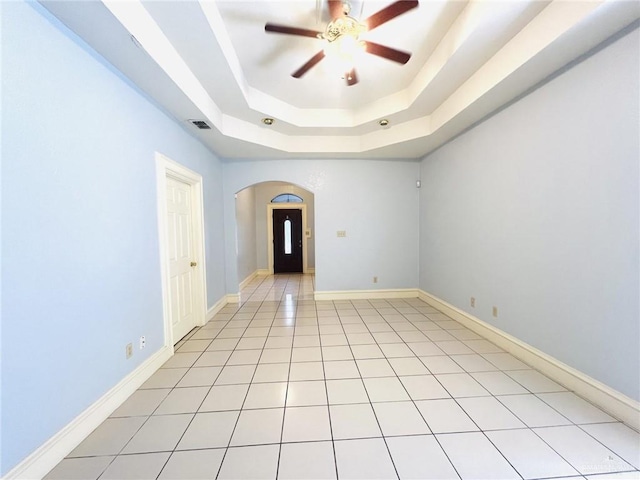 spare room featuring a raised ceiling, ceiling fan, and light tile patterned flooring