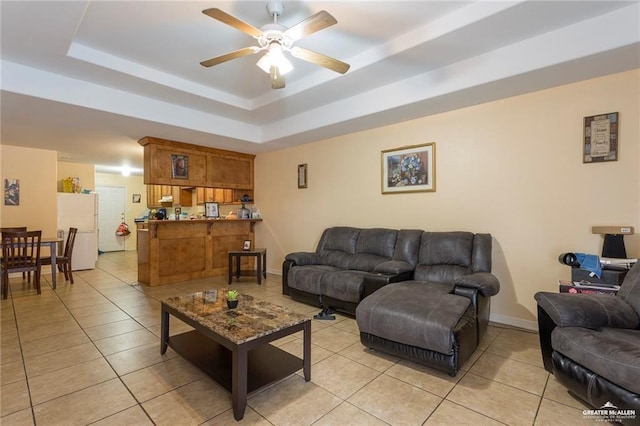 living room featuring a raised ceiling, ceiling fan, and light tile patterned floors