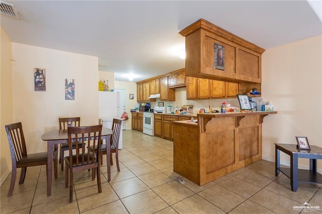 kitchen with a breakfast bar area, kitchen peninsula, light tile patterned flooring, and white appliances