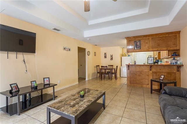 living room featuring ceiling fan, light tile patterned flooring, and a tray ceiling