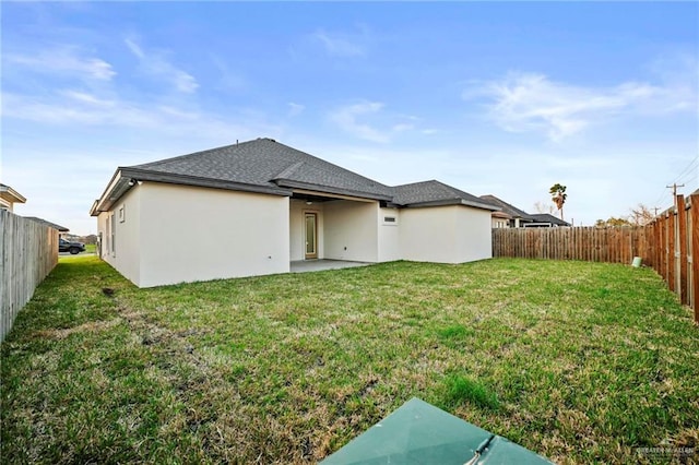 rear view of property featuring a lawn, a fenced backyard, roof with shingles, and stucco siding