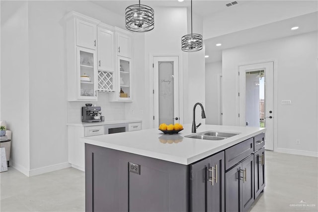 kitchen with white cabinets, light countertops, a sink, pendant lighting, and glass insert cabinets