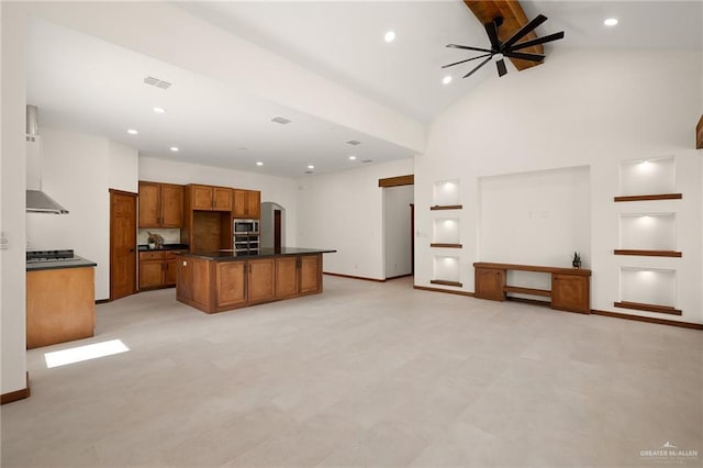 kitchen featuring high vaulted ceiling, an island with sink, wall chimney exhaust hood, ceiling fan, and built in shelves