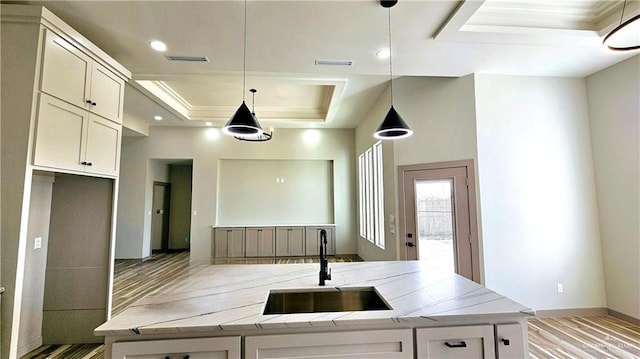 kitchen with a raised ceiling, visible vents, a kitchen island with sink, a sink, and light stone countertops