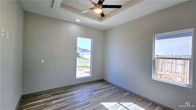 spare room featuring a ceiling fan, a tray ceiling, baseboards, and wood finished floors