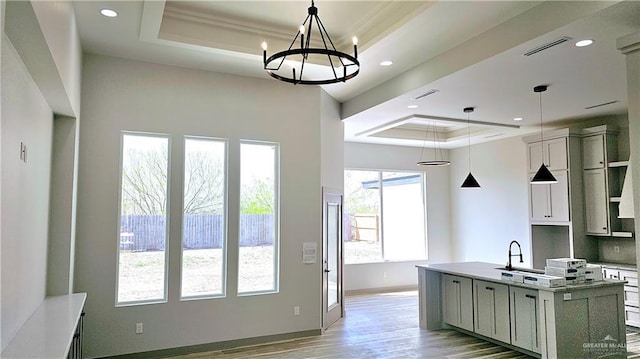 kitchen featuring baseboards, a raised ceiling, decorative backsplash, light wood-style flooring, and a kitchen island with sink