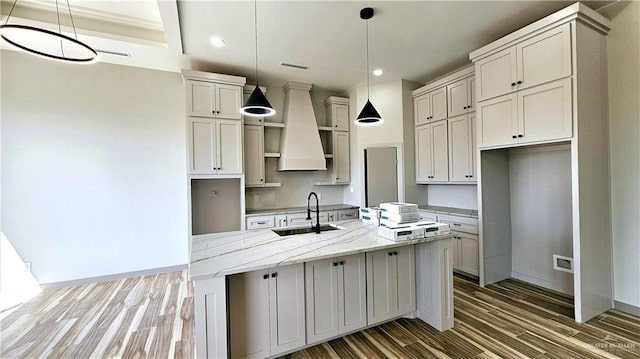 kitchen with a kitchen island with sink, wood finished floors, a sink, baseboards, and custom exhaust hood