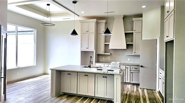 kitchen featuring wood finished floors, custom exhaust hood, a sink, and a kitchen island with sink