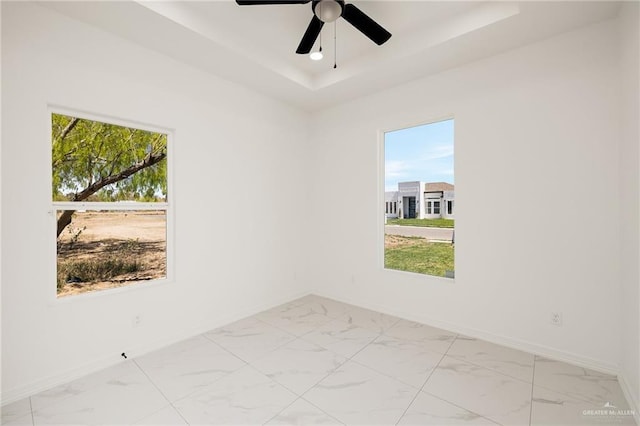 unfurnished room with marble finish floor, baseboards, a tray ceiling, and ceiling fan