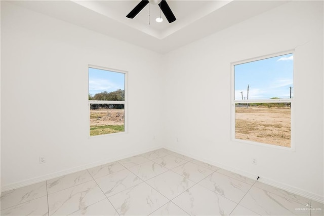 unfurnished room featuring a tray ceiling, baseboards, marble finish floor, and ceiling fan