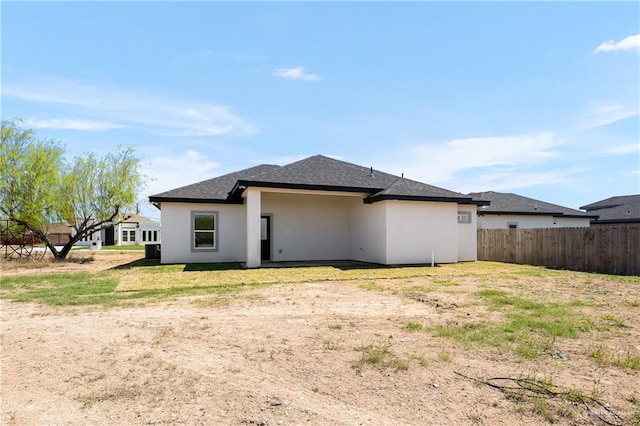 rear view of property with stucco siding, a shingled roof, and fence