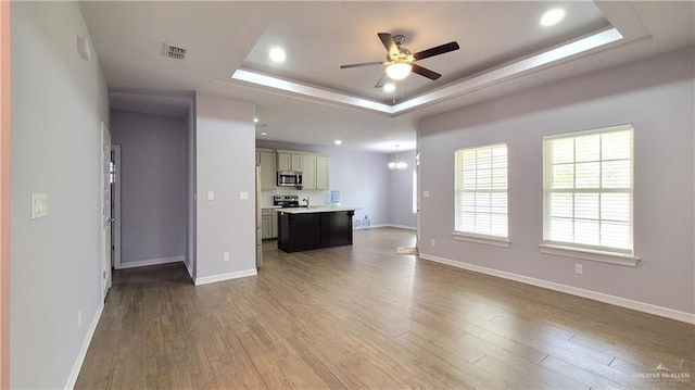 unfurnished living room featuring ceiling fan with notable chandelier, wood-type flooring, and a tray ceiling