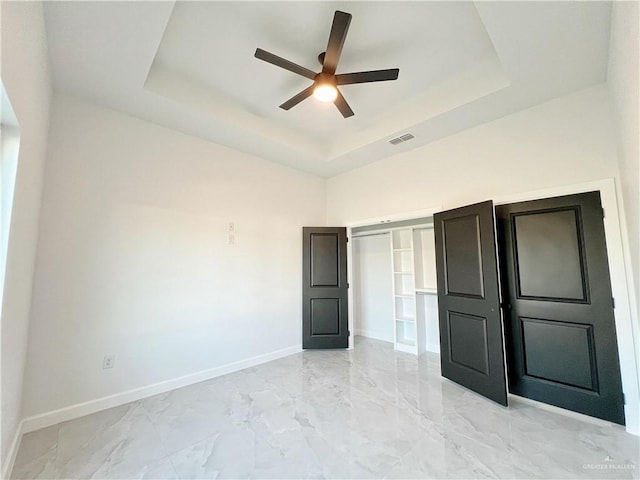 unfurnished bedroom with a closet, a tray ceiling, and ceiling fan