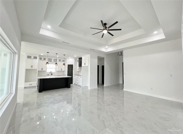 unfurnished living room with a raised ceiling, ceiling fan, and sink