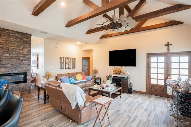 living area with light wood finished floors, visible vents, beam ceiling, and a stone fireplace