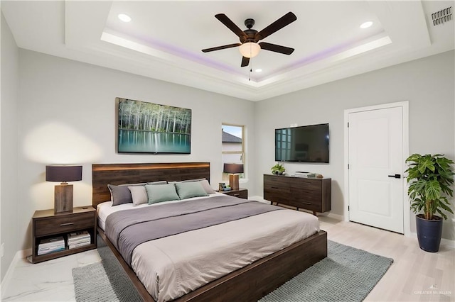 bedroom with a raised ceiling, ceiling fan, and light hardwood / wood-style flooring