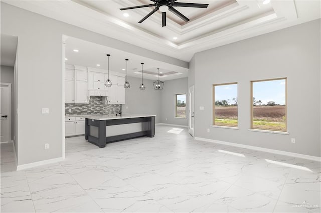 kitchen featuring white cabinetry, a tray ceiling, pendant lighting, ceiling fan, and a kitchen island with sink