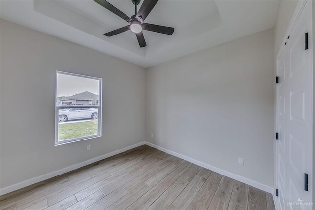 unfurnished room with ceiling fan, light hardwood / wood-style flooring, and a raised ceiling