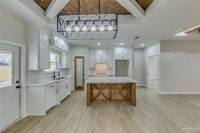 kitchen with white cabinetry, light hardwood / wood-style floors, a kitchen island, pendant lighting, and sink