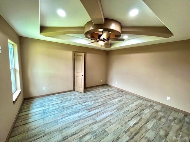 empty room with a tray ceiling, ceiling fan, and light hardwood / wood-style floors