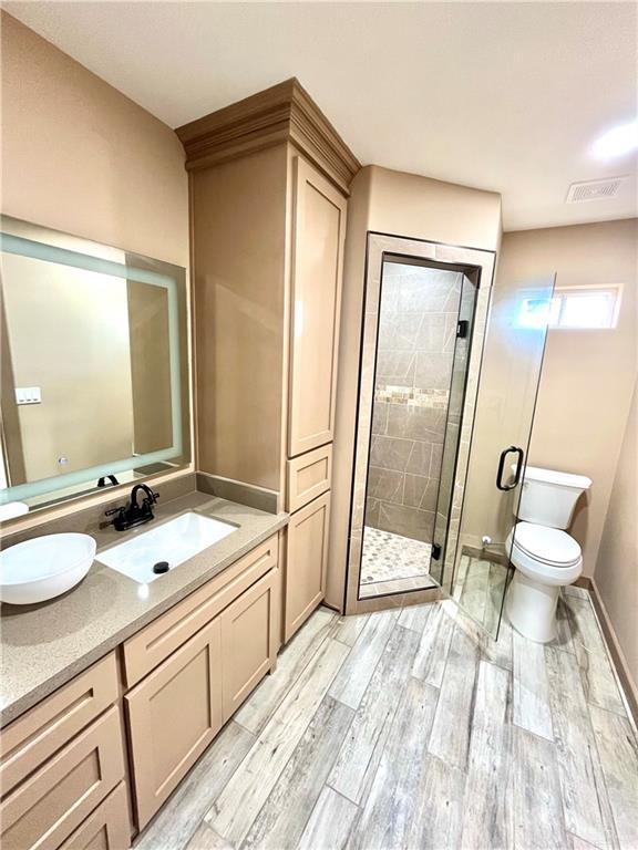 bathroom with hardwood / wood-style floors, vanity, an enclosed shower, and toilet